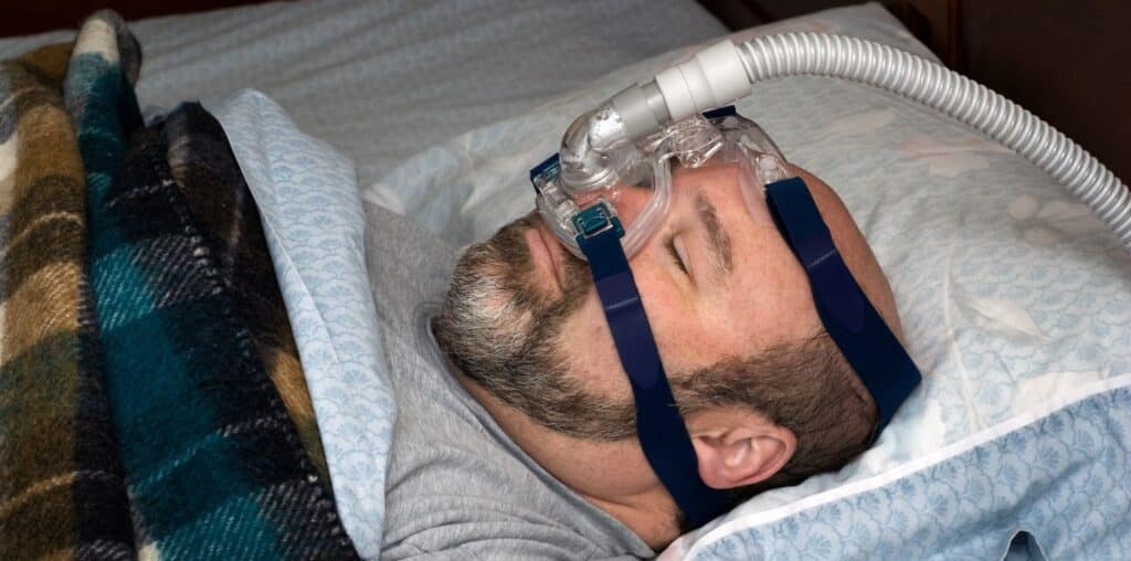 Man wearing a CPAP mask while sleeping in bed